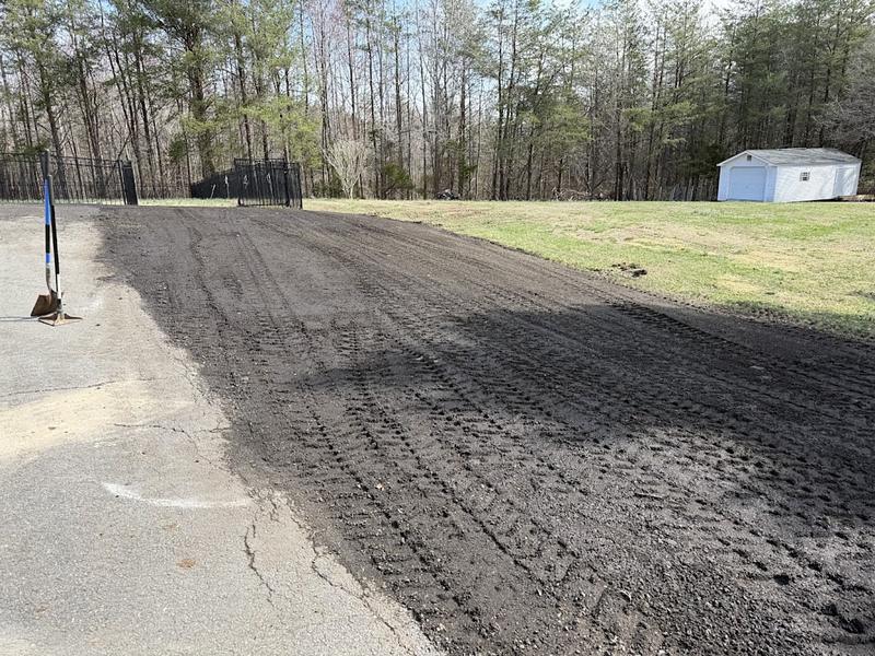 Finished driveway shoulder, topsoil spread smooth and graded flush with the asphalt edge