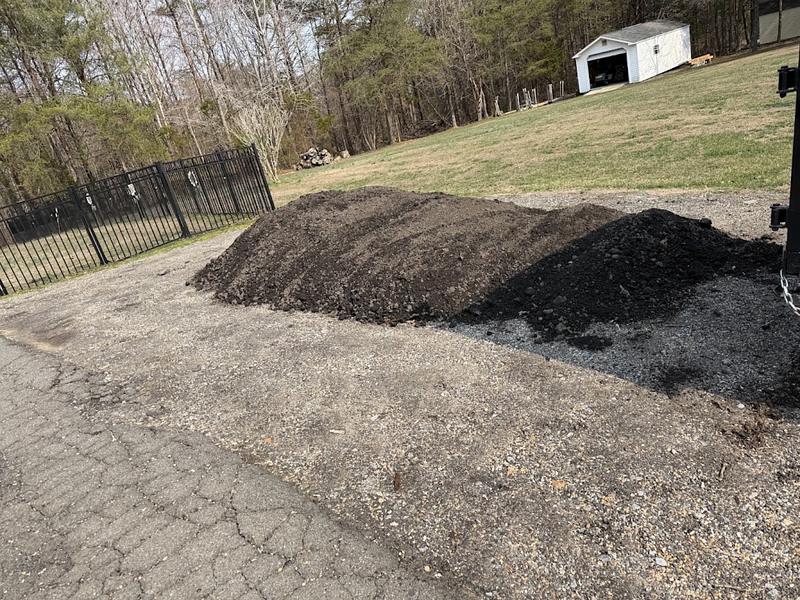 Load of dark screened topsoil dropped alongside an asphalt driveway before spreading