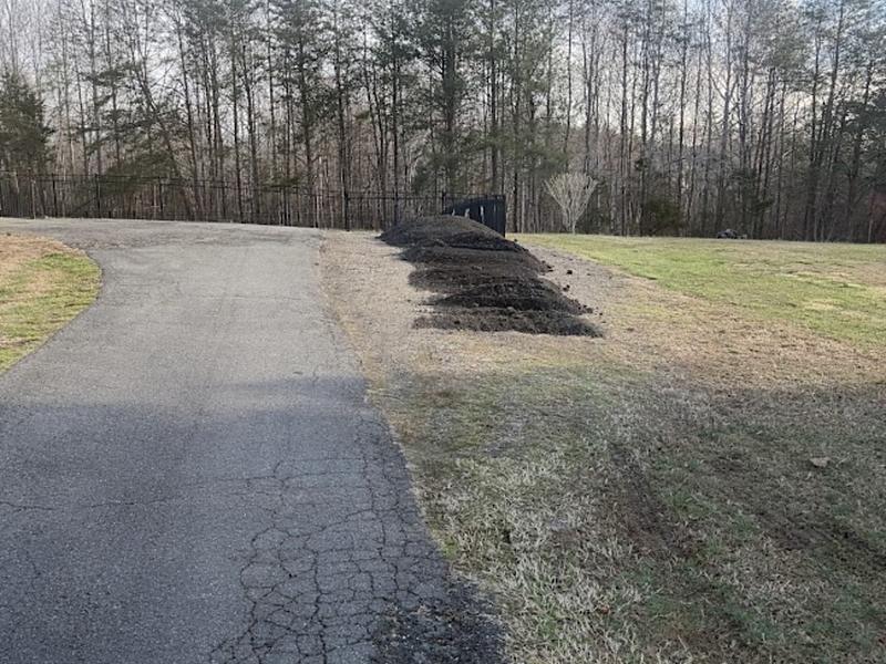 Topsoil windrowed in a long row down the edge of an asphalt driveway, ready to be spread