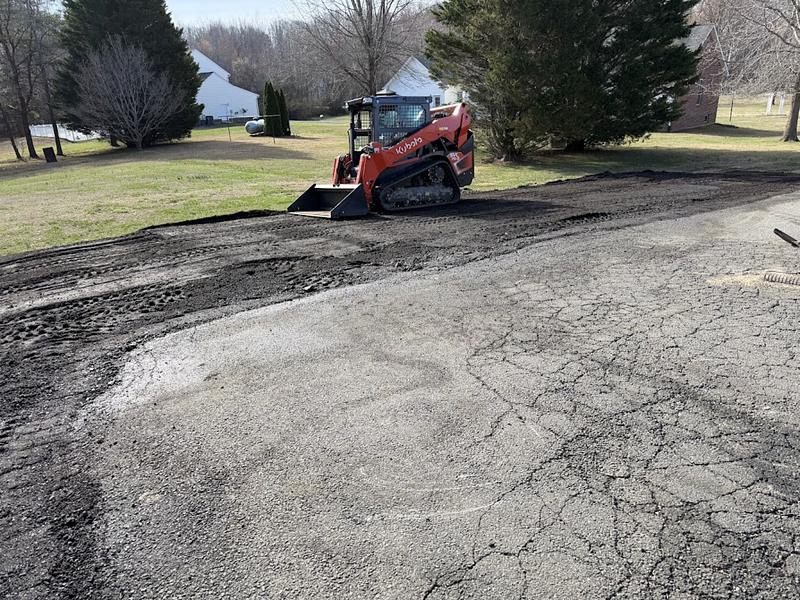 Kubota track loader spreading and shaping topsoil along the shoulder of an asphalt driveway