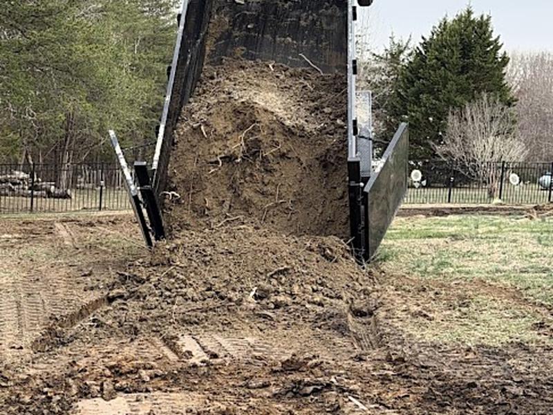 Dump trailer tipped up, releasing a load of fill soil onto a graded area of the yard