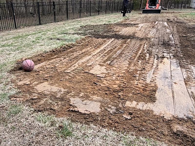 Track loader shaping a rectangular pad of bare graded soil, track marks visible across the surface